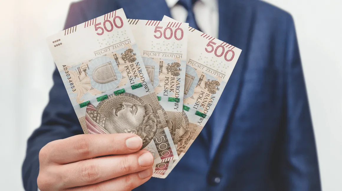 Mężczyzna w niebieskim garniturze trzyma banknoty 500 zł