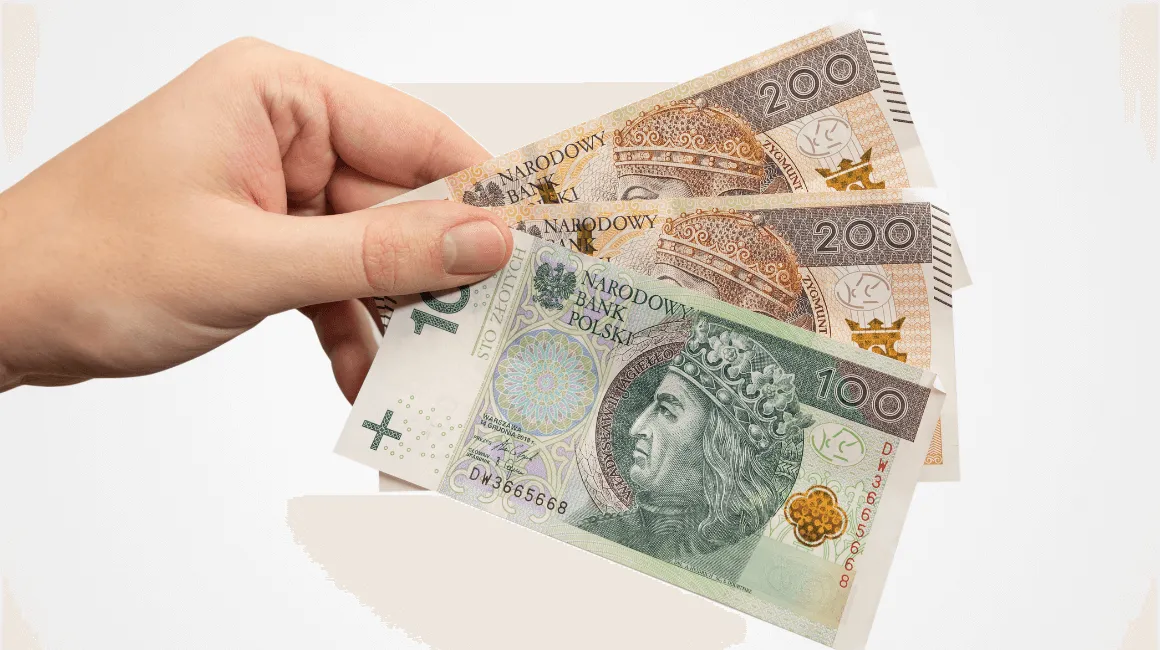 Osoba trzyma w dłoni banknoty 100 i 200 zł
